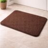 Brown anti-skid bath mat placed on a tiled bathroom floor near a door with a soft textured surface