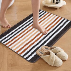 Black, brown, and white striped soft bathroom mat placed on a wooden floor, with slippers beside it.