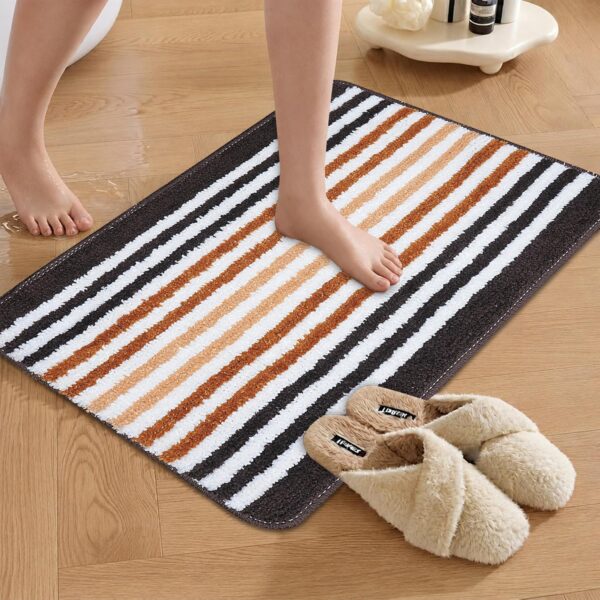 Black, brown, and white striped soft bathroom mat placed on a wooden floor, with slippers beside it.
